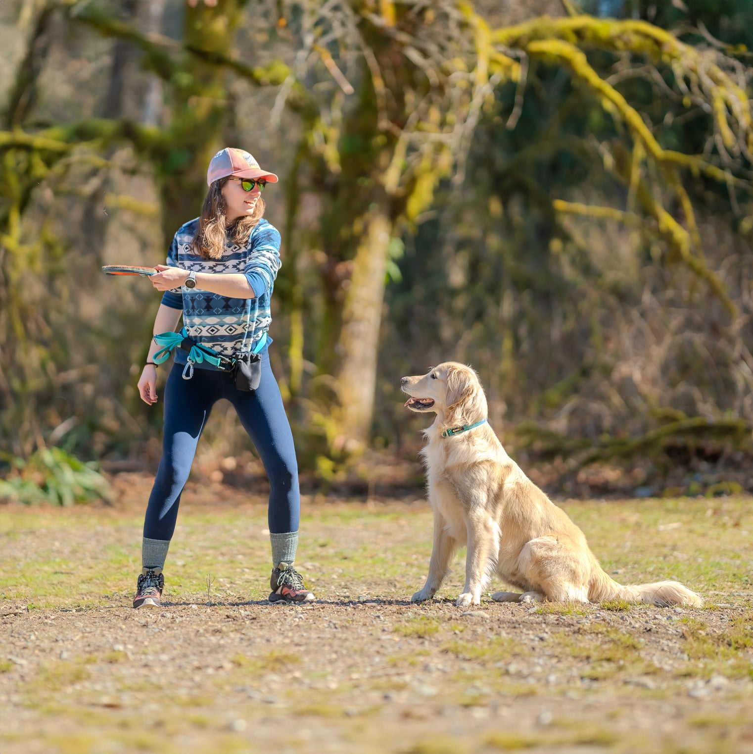 A woman playing fetch with her dog with a DogGo Padded Adjustable Leash stored in the leash holder of the Hands-Free Adventure Belt, in glacier teal.